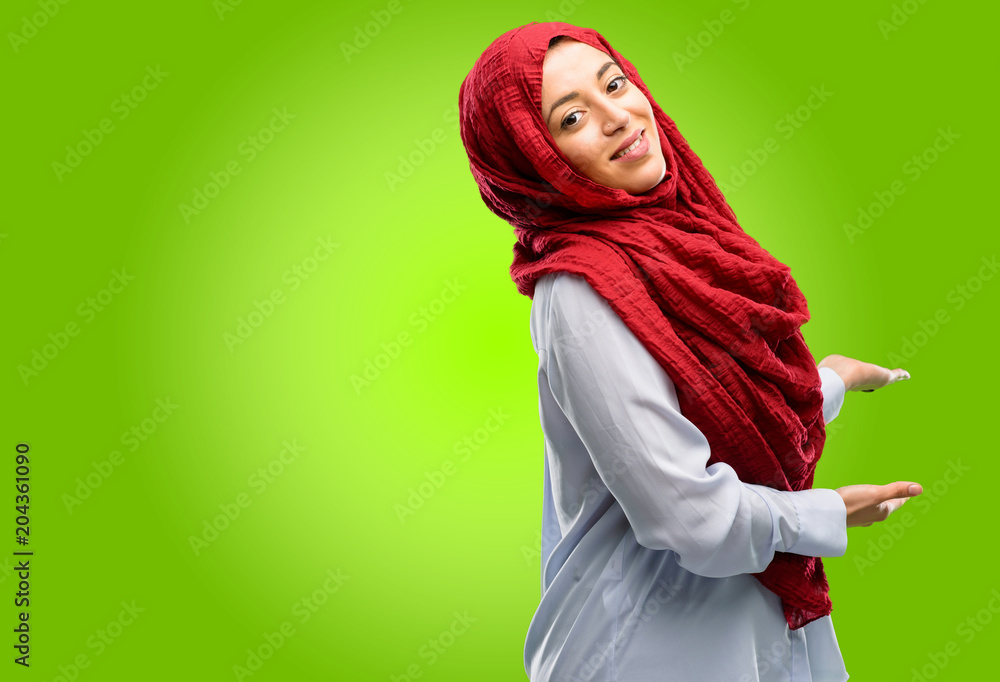 Young arab woman wearing hijab confident and happy with a big natural smile inviting to enter Young arab woman wearing hijab confident and happy with a big natural smile inviting to enter