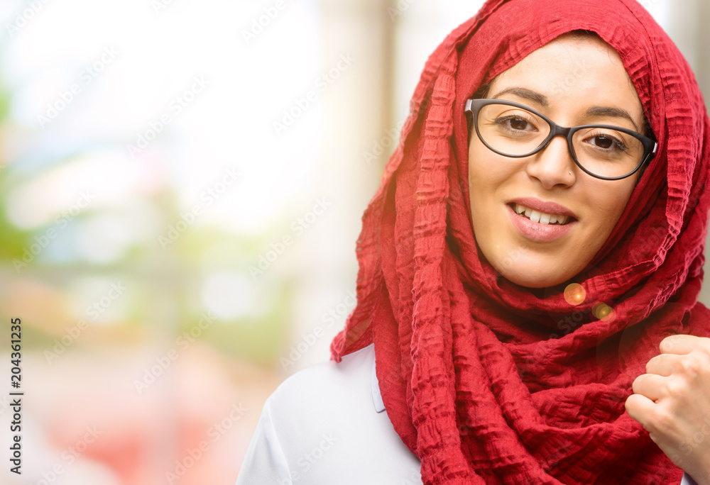 Young arab woman wearing hijab smiling broadly showing thumbs up gesture to camera, expression of like and approval Young arab woman wearing hijab smiling broadly showing thumbs up gesture to camera, expression of like and approval