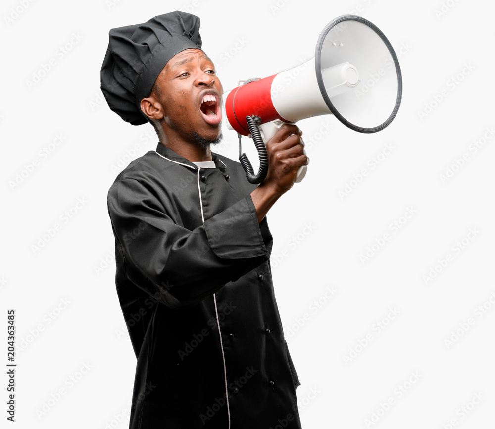 Young black cook wearing chef hat communicates shouting loud holding a megaphone, expressing success and positive concept, idea for marketing or sales Young black cook wearing chef hat communicates shouting loud holding a megaphone, expressing success and positive concept, idea for marketing or sales