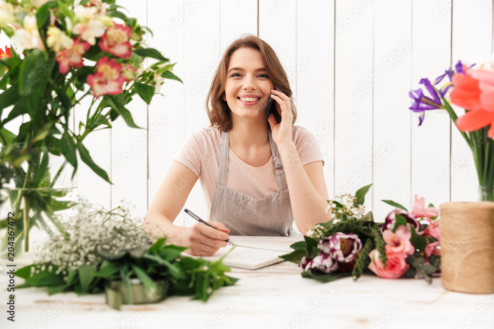 Cute happy florist lady over flowers in workshop Cute happy florist lady over flowers in workshop