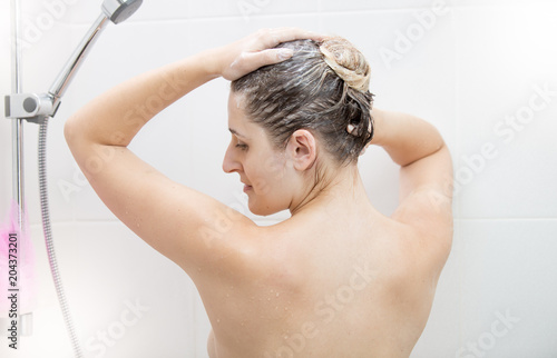 Portrait of beautiful young woman washing long dark hair in shower