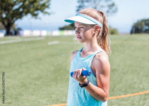 Sporty girl standing with small weight in her hand side profile on sports field.