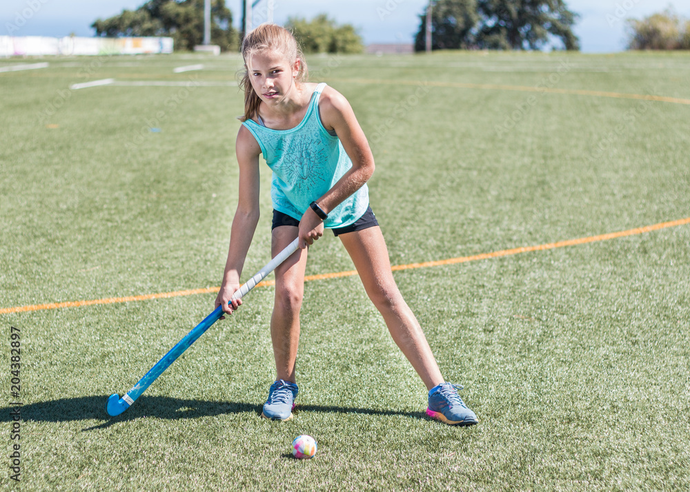 Sporty girl standing looking at camera making ready to hit a hockey ball on sports field.
