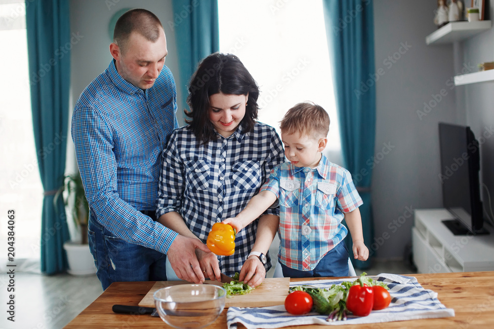 Family mom, dad and son cooking red green and yellow vegetables at the table in the kitchen