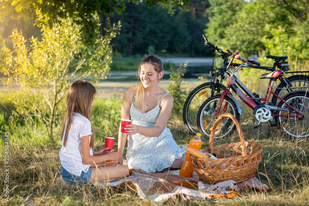 Happy young family sitting on blanket under tree and having picnic Happy young family sitting on blanket under tree and having picnic