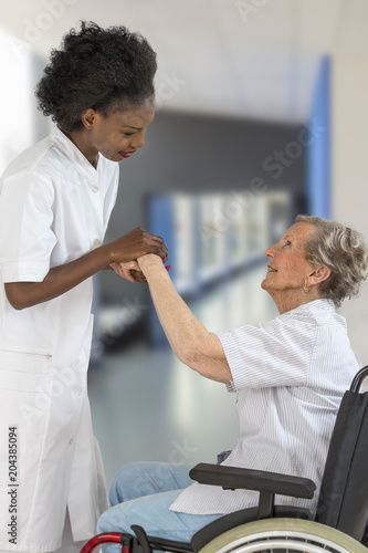 Careful female caregiver or nurse helping senior woman to stand up