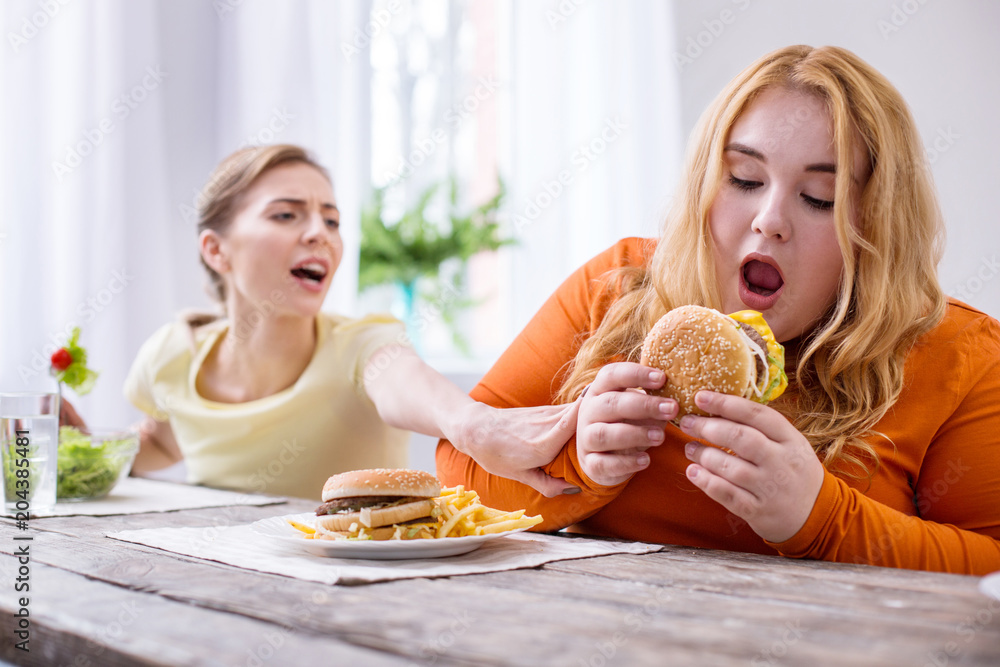 So tasty. Weak-willed overweight woman eating a sandwich and her friend stopping her So tasty. Weak-willed overweight woman eating a sandwich and her friend stopping her