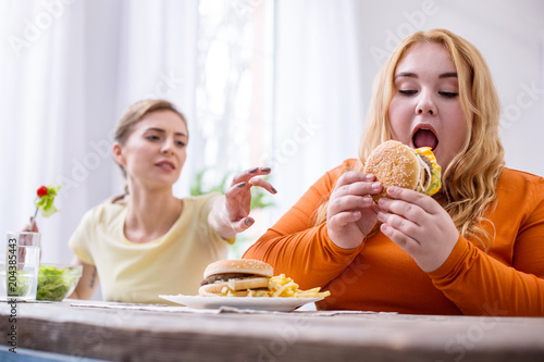 So delicious. Weak-willed plump woman eating a sandwich and her friend stopping her