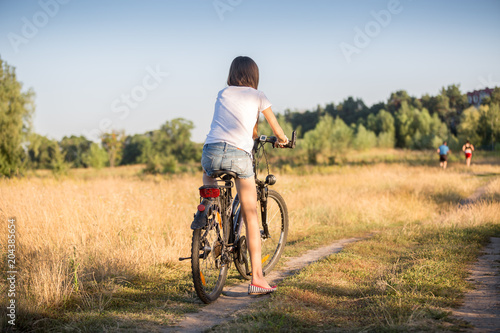 Rear view image of young girl riding bicycle on countryside road