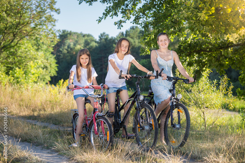 Young smiling mother riding bicycle with two daughters at field