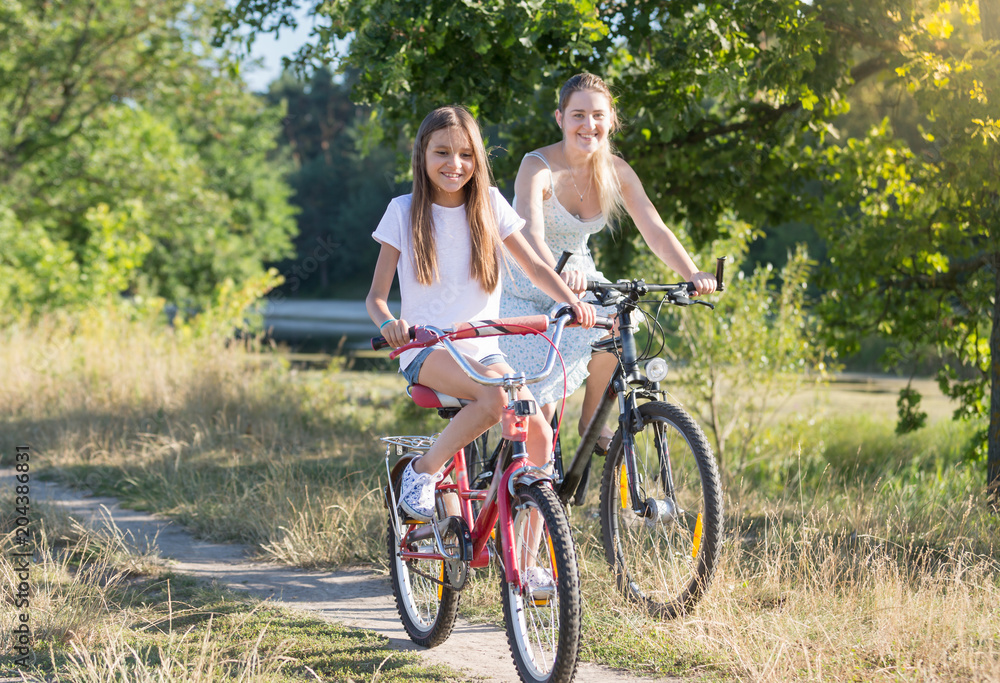 Happy smiling girl riding bicycle with young mother in field at hot summer day Happy smiling girl riding bicycle with young mother in field at hot summer day
