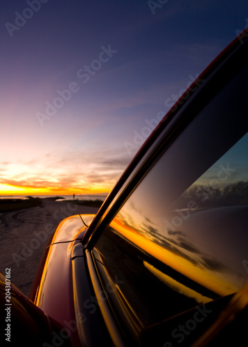 sunrise on the coast with car silhouette and reflections of sunrise on windows