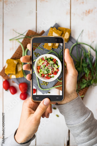 Phone photography of food. Woman hands take photo of lunch with smartphone for social media. Fresh vegetables salad. Raw vegan vegetarian healthy dinner 