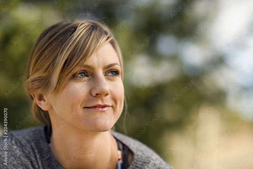 Smiling young woman looks thoughtfully into the distance as she sits outside. Smiling young woman looks thoughtfully into the distance as she sits outside.
