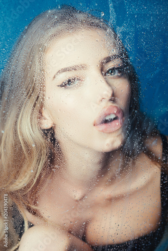 Rain drops on window glass with face of girl. Fashion and beauty. Window with water drops before girl with makeup. Sexy woman behind plastic sheet with water drops. Shower and hygiene spa treatment