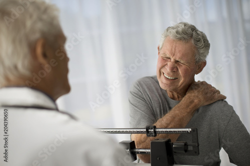 Mature man grips his shoulder in pain while attending a medical examination. photo