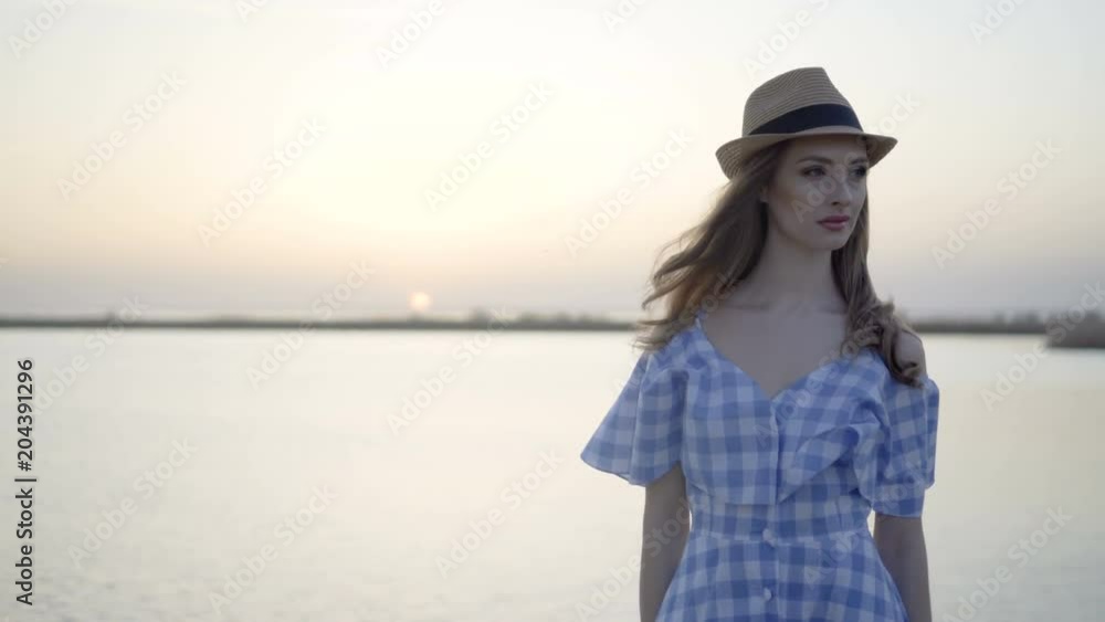 Attractive woman in hat and dress is sitting and looking at sunset Attractive woman in hat and dress is sitting and looking at sunset