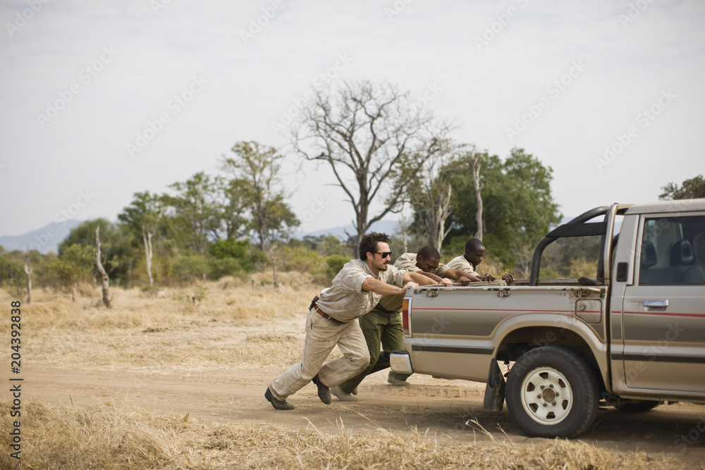 © Erickson Stock - Three mid-adult men pushing a truck along a dirt road. © Erickson Stock - Three mid-adult men pushing a truck along a dirt road.