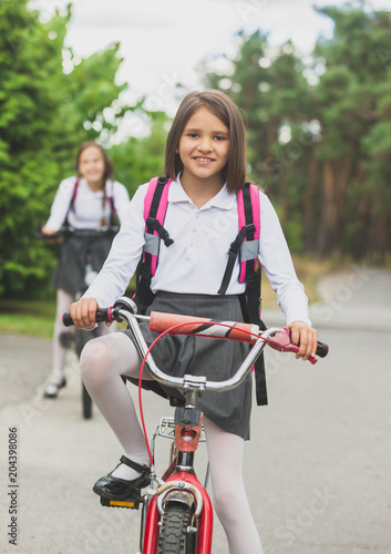 Portrait of beautiful girl in school uniform and bag riding to school on bicycle