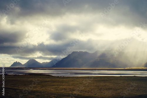 Beautiful mountains in a fog, moss fields, overcast weather with rays of the light. Scenic landscape in Southeast Iceland at the sunset.