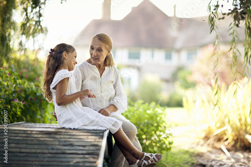 Young girl sits on a footbridge talking to her grandmother.