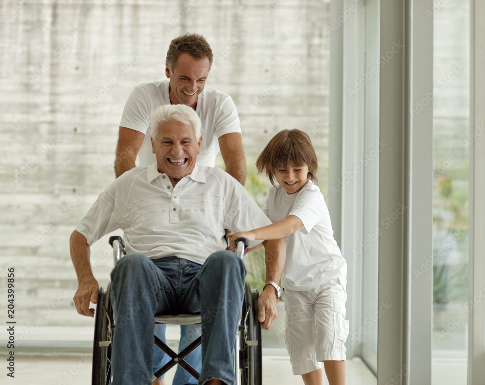 Senior man being pushed in wheelchair, by his adult son and his grandson. Senior man being pushed in wheelchair, by his adult son and his grandson.