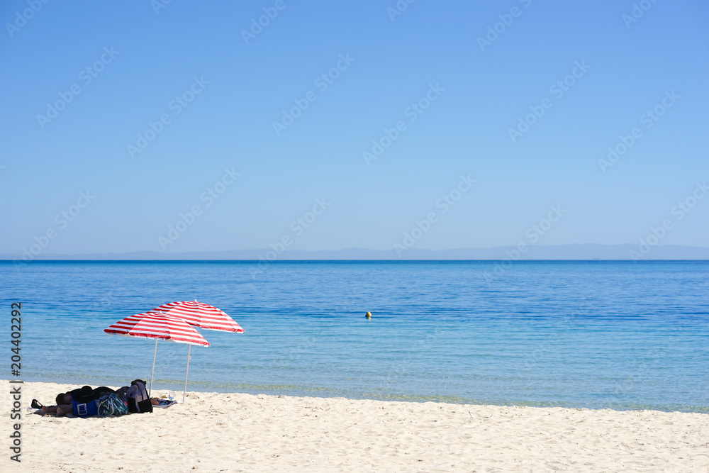 A couple is resting at the beach. Selective focus on the red and white beach umbrella.
