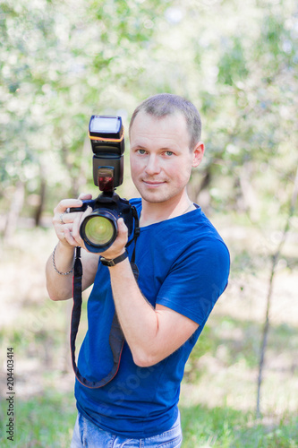 Portrait of attractive male photographer wearing blue t-shirt outdoors on Summer day. Young man with a DSLR camera in hands © dxoroshun