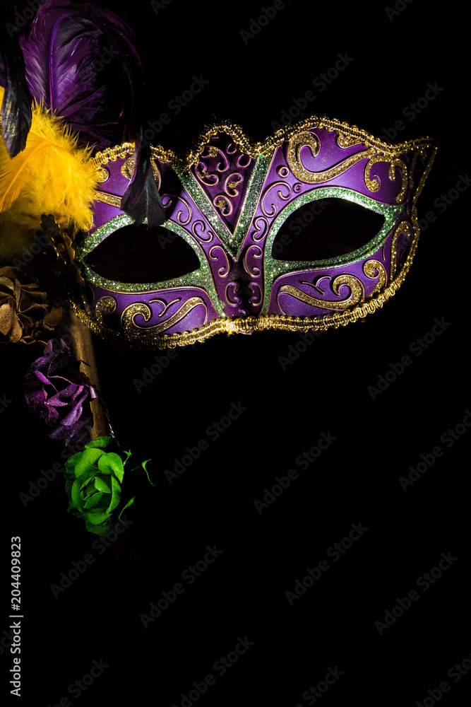 A purple mardi gras or venitian mask with feathers and flowers on a black background with copy space