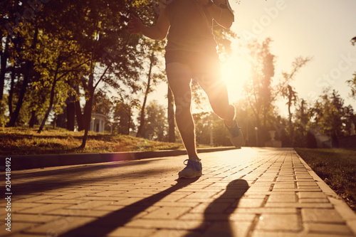 A male runner is running down the road in the park at sunset.