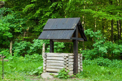 genuine wooden well with black roof in the forest, concept of authentic objects in the wild, copy space, close-up