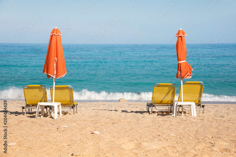 Abstract image with sun loungers and orange umbrellas from the sun on the beach on the seafront with waves (relaxation, harmony, holidays - concept) Abstract image with sun loungers and orange umbrellas from the sun on the beach on the seafront with waves (relaxation, harmony, holidays - concept)
