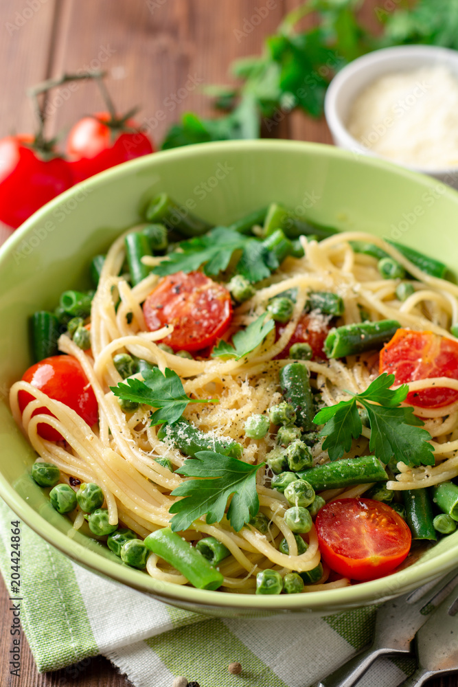 Spaghetti pasta with green beans, peas, cherry tomatoes, parsley and parmesan cheese on wooden table Spaghetti pasta with green beans, peas, cherry tomatoes, parsley and parmesan cheese on wooden table