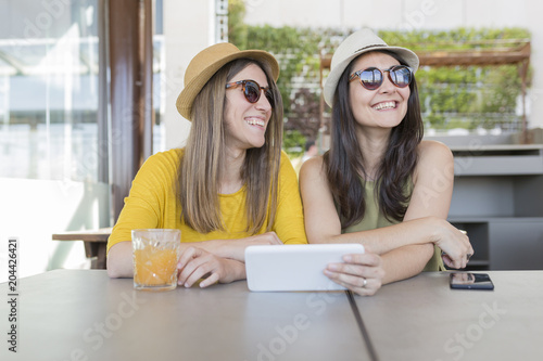 two beautiful women having breakfast in a restaurant. They are laughing and searching information on a tablet. Indoors lifestyle and friendship concept © Eva