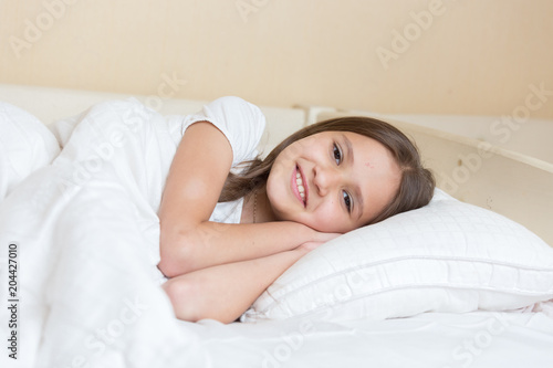 Closeup portrait of beautiful smiling girl lying on pillow at bed