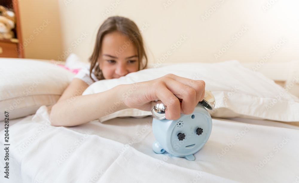 Closeup image of angry teenage girl lying on bed and turning off alarm clock Closeup image of angry teenage girl lying on bed and turning off alarm clock