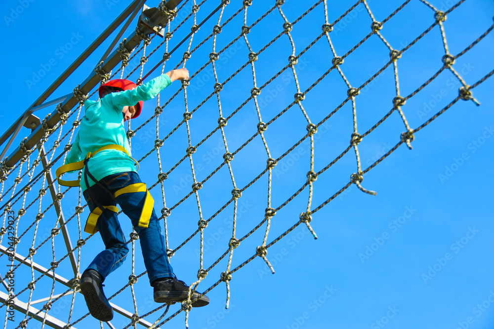 Teenager boy moves the vertical grid on the obstacle course in the amusement park, outdoor activities, rock climbing, danger, training, height, fear, copy space