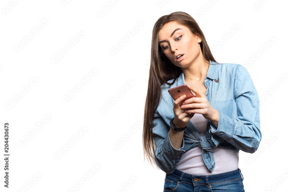 Portrait of a young brunette woman looking at the smartphone in her hands surprised against white background, isolated. Lifestyle, people and technology concept Portrait of a young brunette woman looking at the smartphone in her hands surprised against white background, isolated. Lifestyle, people and technology concept