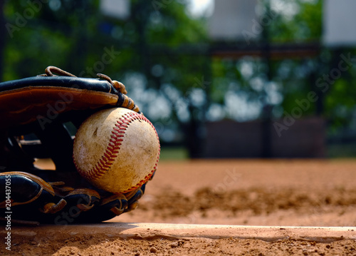 Baseball in glove laying on pitcher's mound of ball field. Old used sports equipment for team sport.