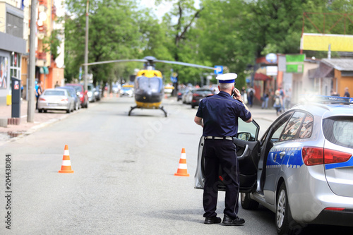 Policjant rozmawia przez telefon przy samochodzie służbowym, przed śmigłowcem w centrum miasta Opola.