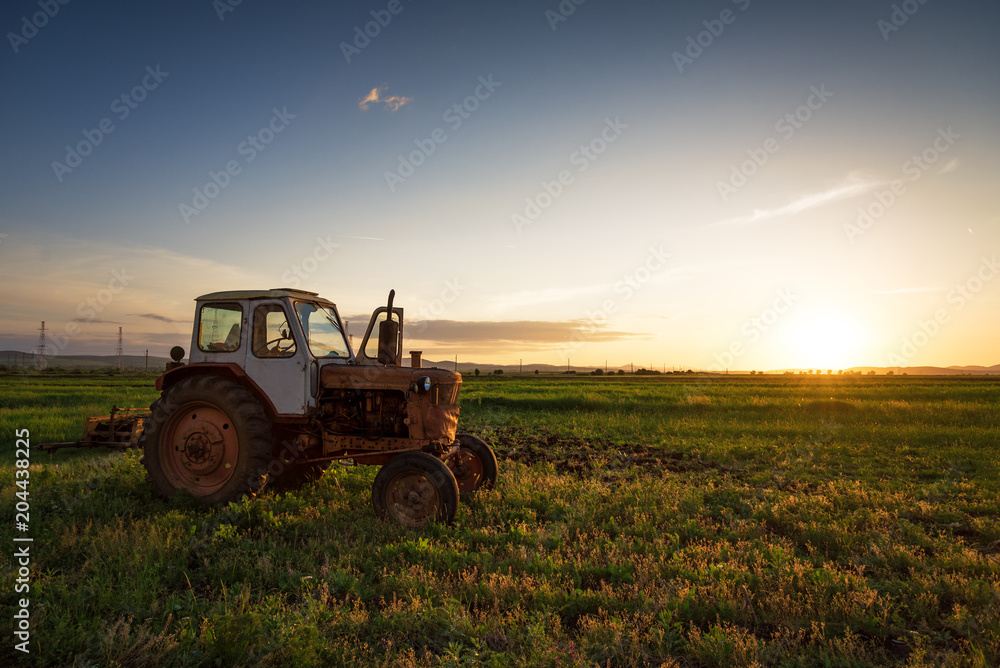 Fototapeta premium Red tractor on golden sunset sky.