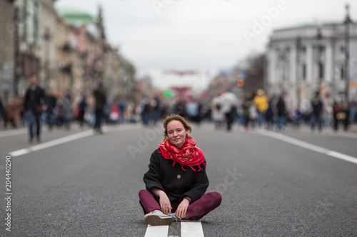 Girl sitting on the road in middle of busy street.