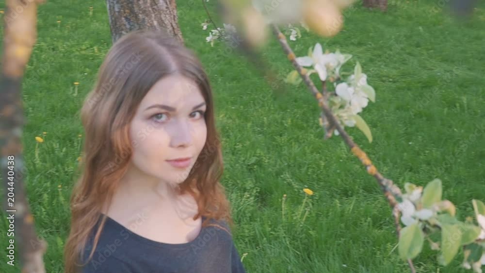 young happy woman walking in an apple orchard in the spring flowers white. Portrait of a beautiful girl young happy woman walking in an apple orchard in the spring flowers white. Portrait of a beautiful girl