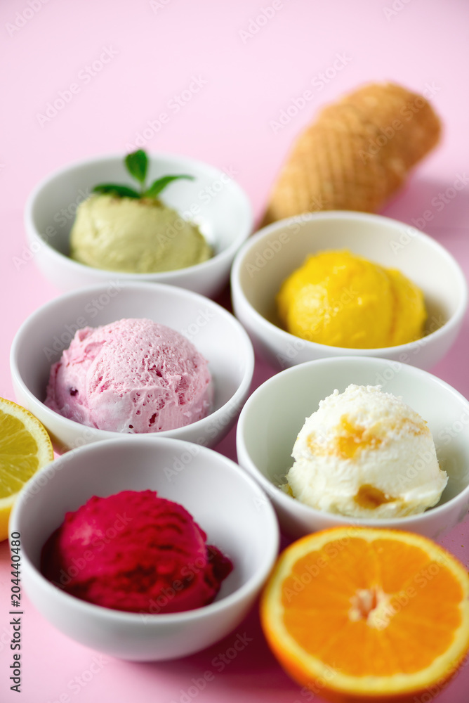 Red, purple, yellow, green, white ice cream balls in bowls, waffle cones, berries, orange, mango, lemon, mint, pistachio, pink shabby chic background. Colorful collection, summer concept Red, purple, yellow, green, white ice cream balls in bowls, waffle cones, berries, orange, mango, lemon, mint, pistachio, pink shabby chic background. Colorful collection, summer concept
