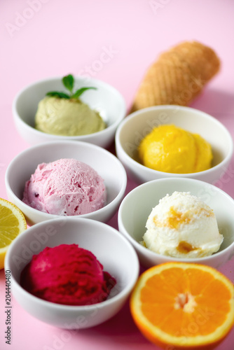 Red, purple, yellow, green, white ice cream balls in bowls, waffle cones, berries, orange, mango, lemon, mint, pistachio, pink shabby chic background. Colorful collection, summer concept