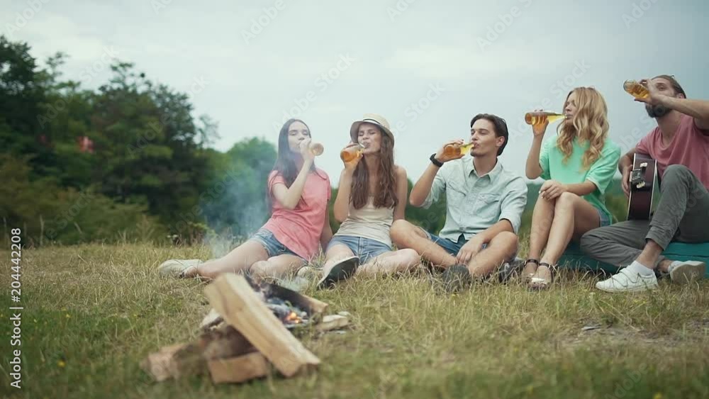 Happy Friends Drinking Beer, Having Fun And Sitting Near Bonfire Happy Friends Drinking Beer, Having Fun And Sitting Near Bonfire