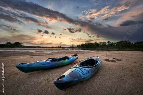 two kayaks sitting on the sand of a beach with a brilliant sunset in the sky