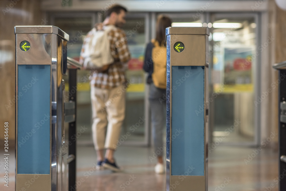 closeup shot of turnstiles and couple of travelers with backpacks behind closeup shot of turnstiles and couple of travelers with backpacks behind