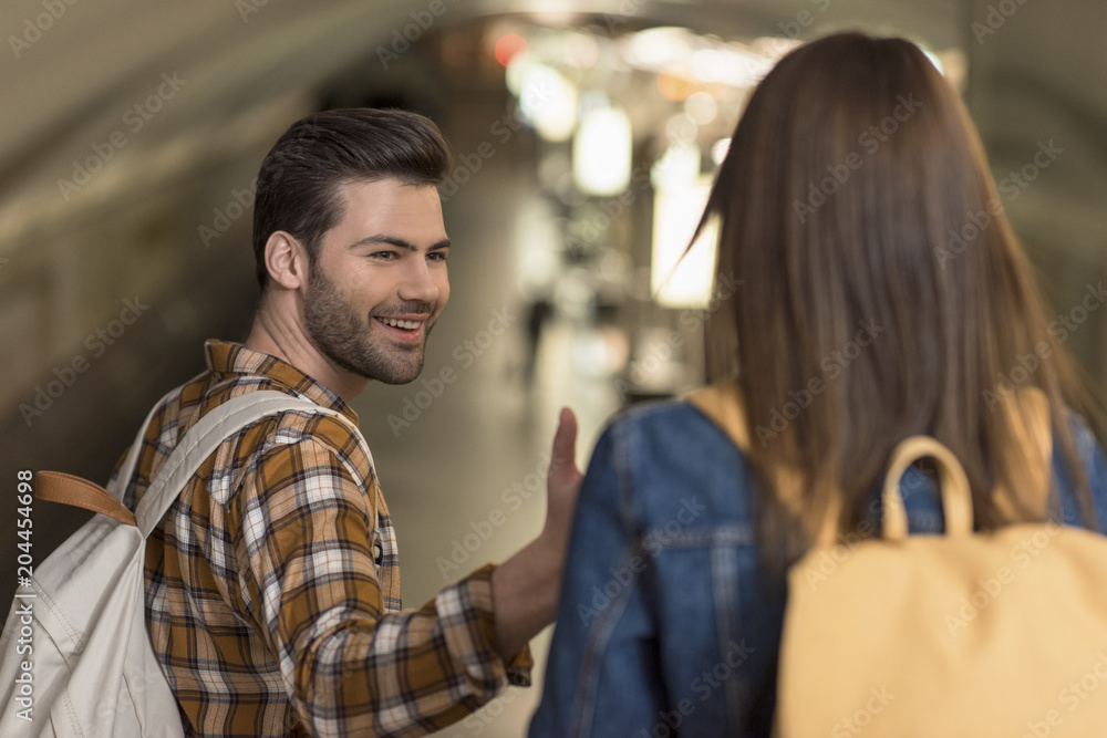 smiling male tourist with backpack giving hand to girlfriend at subway station smiling male tourist with backpack giving hand to girlfriend at subway station