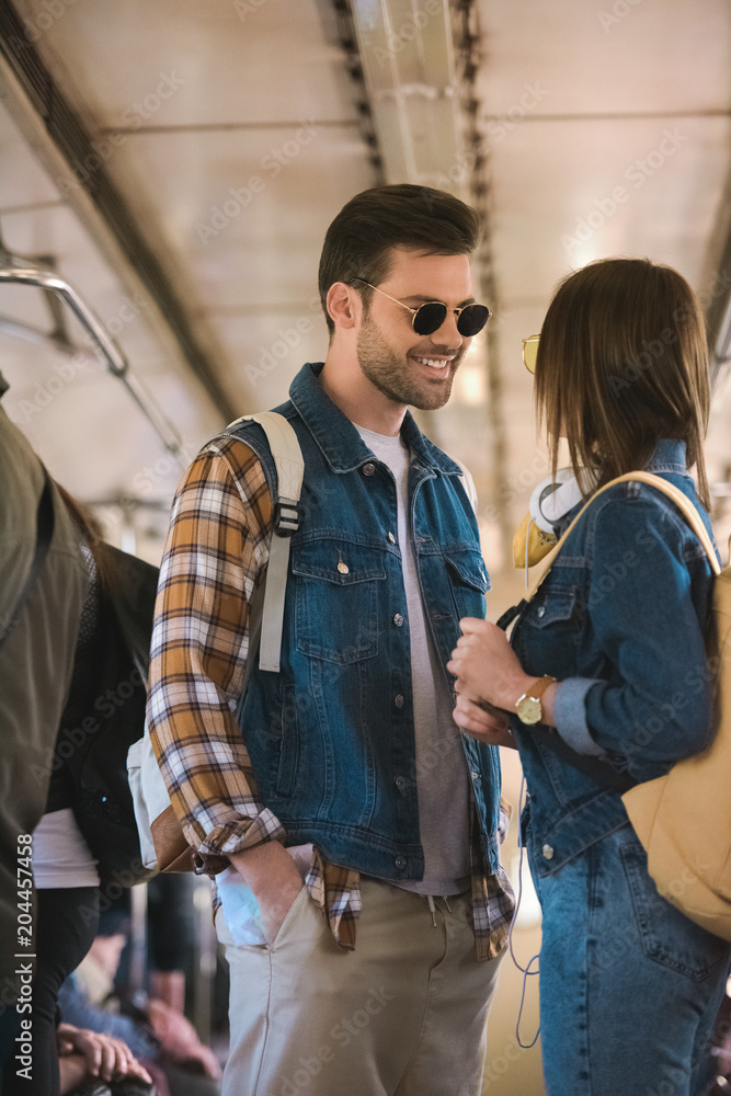 smiling male traveler in sunglasses talking to girlfriend in metro train